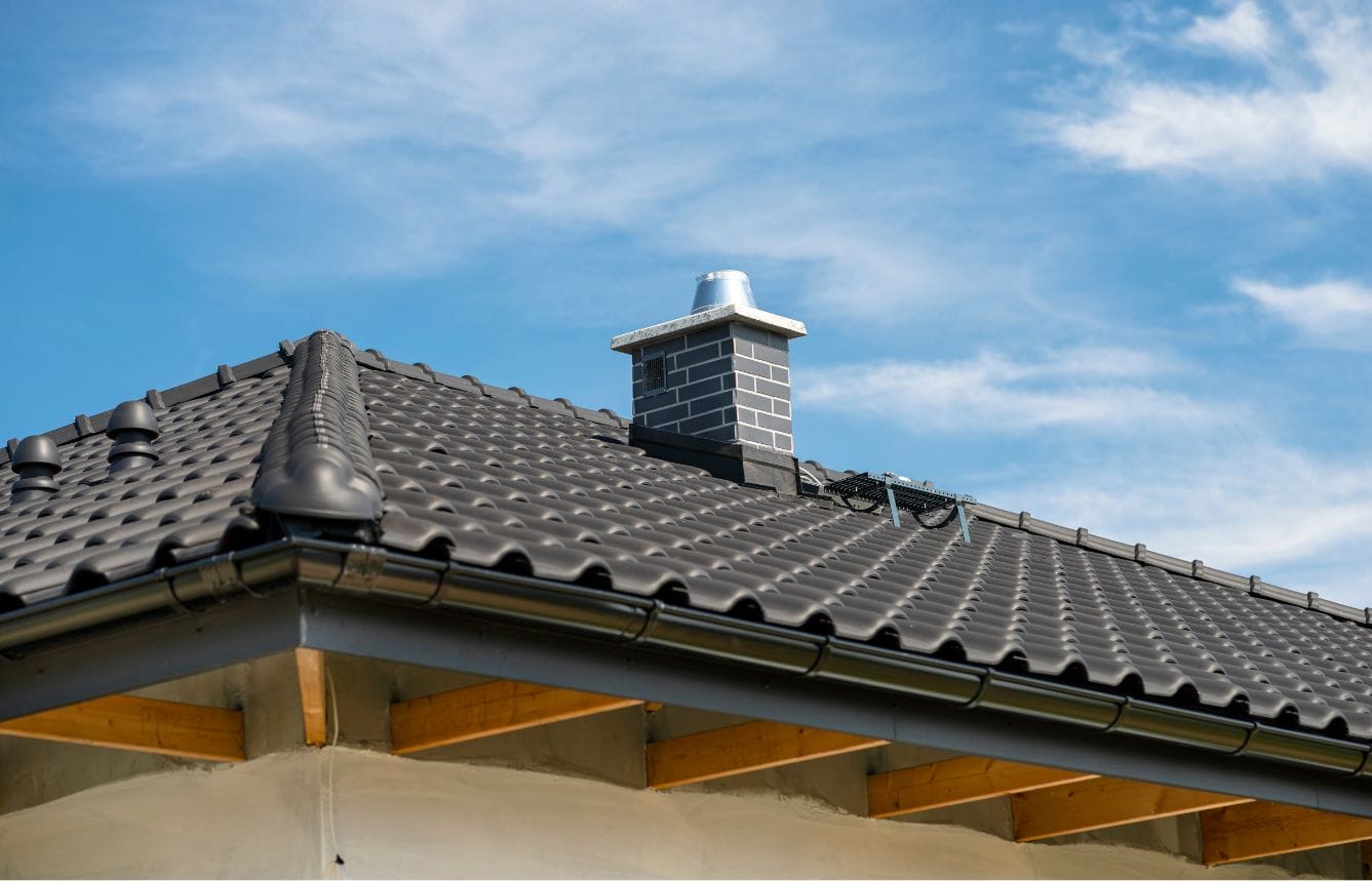 Modern sloped roof with chimney under blue sky.